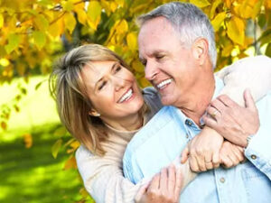 Two mature adults smiling at each other with restored teeth.
