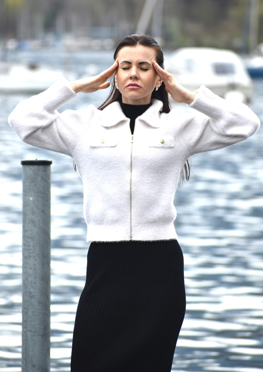 Seattle woman stands by the docks holding her head with her hands with a severe migraine